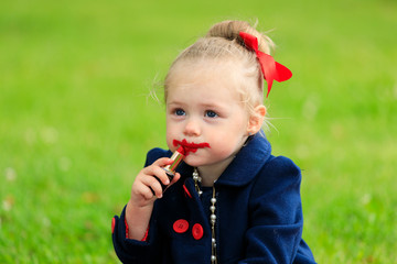 Canvas Print - the child sits and paints his lips with red lipstick