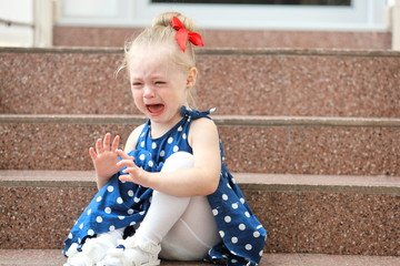 Wall Mural - little girl in a blue dress sits on the steps and cries