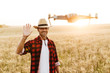 © Drobot Dean - Image of happy man using drone while waving hand at cereal field