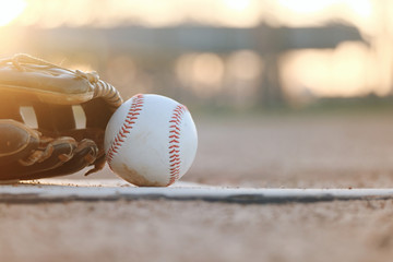 Wall Mural - baseball and glove on field during sunset close up, blurred background