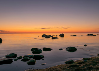 Wall Mural - orange sunset by the sea, black stone silhouettes against the sea background, summer