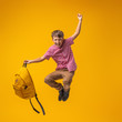mischievous schoolboy with backpack jumps on yellow background