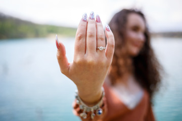 Wall Mural - Image of a girl a silver wedding ring on a woman's hand, outdoors. Sea or river background