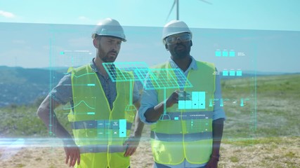 Two Interracial Engineers in Reflective Vests Helmets Examine Efficiency Data of Windmill Ecological Factory on Holographic Touchscreen. Virtual Reality. Alternative Energy. Ecology and Technology.