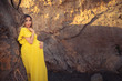 young pregnant girl on brown rocks view in yellow dress 