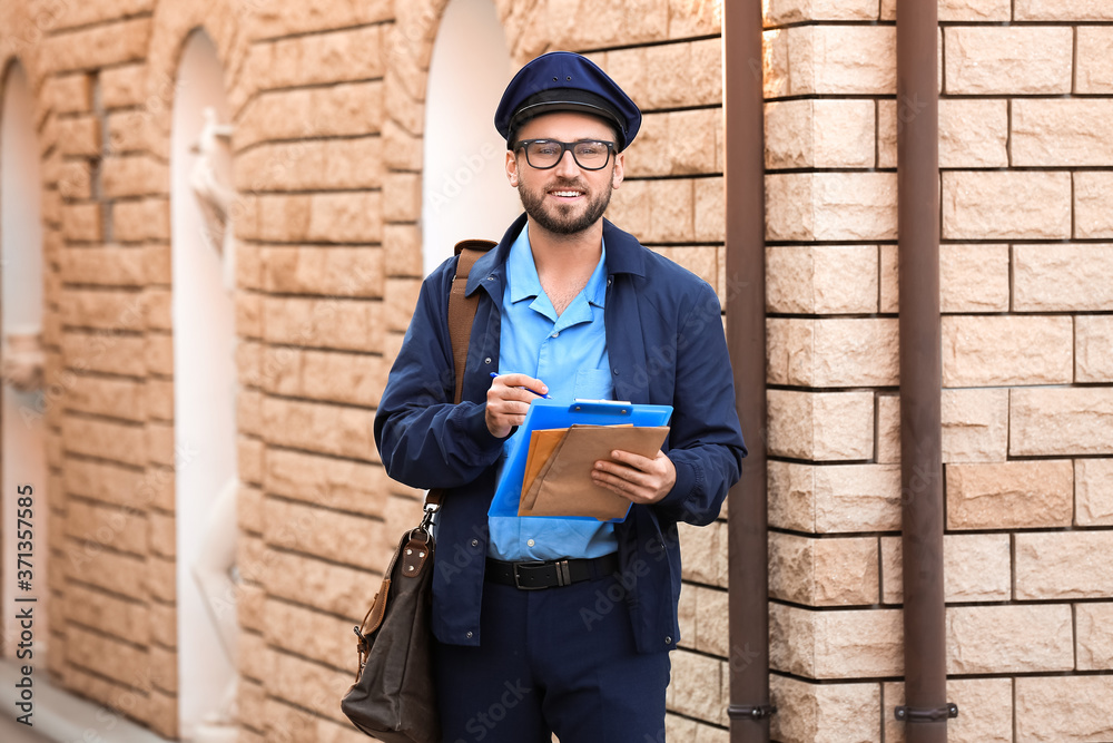 Handsome young postman with letters outdoors