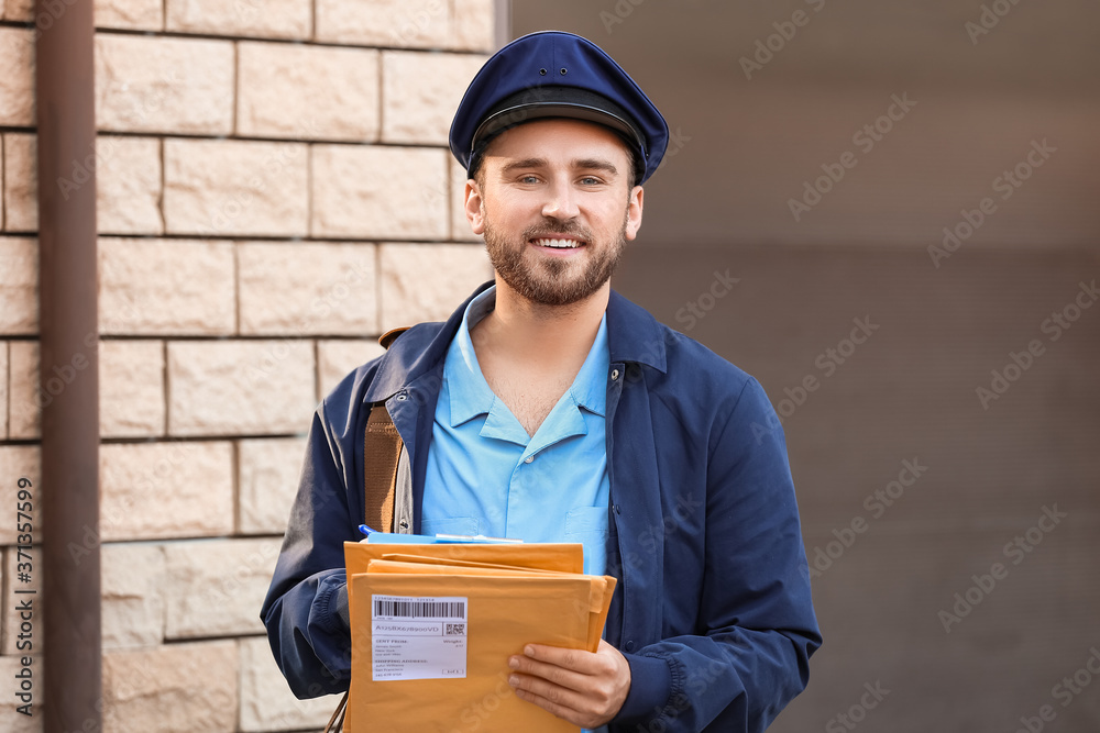 Handsome young postman with letters outdoors