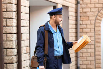 Wall Mural - Handsome young postman with letters outdoors