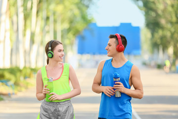 Sticker - Sporty young couple with headphones drinking water outdoors