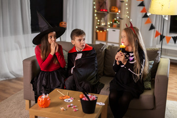 Sticker - halloween, holiday and childhood concept - smiling boy and girls in party costumes playing with flashlight and scaring each other at home