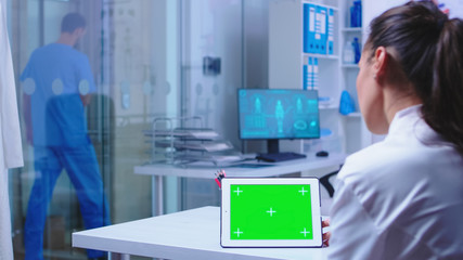 Chroma key on tablet pc display used by doctor in hospital cabinet and nurse leaving the clinic wearing blue uniform. Doctor in health clinic working on tablet computer with replaceable screen doing