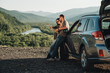 © Romvy - Travelers Couple on a Road Trip, Man and Woman Using Map on Journey Near Their Car Over Beautiful Landscape
