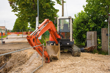 A compact crawler excavator with a rotating house platform and continuous caterpillar track on a sewer replacement work site in north west Italy
