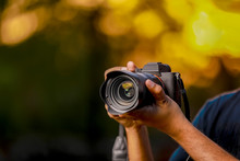 Closeup Of A Black Camera Holding By Photographer's Hand With Sunset Background