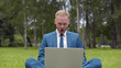© TommyStockProject - Handsome man in formal wear sitting outdoors in grass surprised watching funny video on laptop
