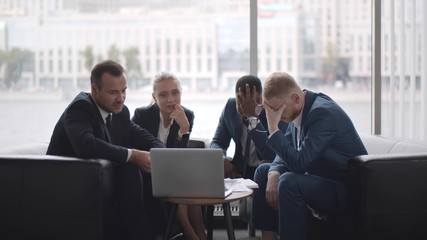 Upset business team analyzing financial data on laptop sitting in business center lobby