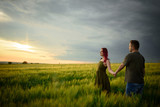 Fototapeta  - Young couple in a wheat field at sunset. Couple spend romantic time together.