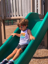 Boy Going Down A Green Slide Now That The Parks Are Open Again.  After Pandemic In Mackel Park In Marco Island Florida 