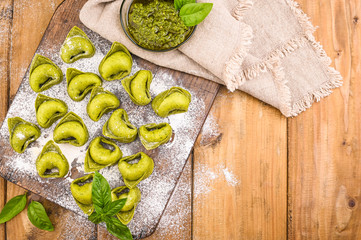 Tortellini e tortelloni typical dishes emilia italy. Food background with homemade raw Italian tortelloni and ingredients for green pesto on wooden background . High angle view. Copy space.