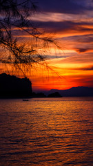 Wall Mural - Sillhoute of two peoples in a boat with a beautiful setting sun behind the hills and rocks with its reflection over the sea waves at Tanjung Rhu Beach, Langkawi,