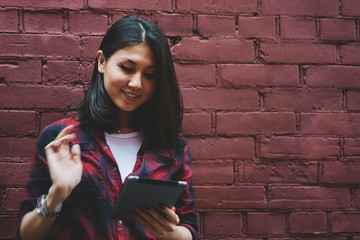 Wall Mural - Happy young hipster girl holding modern digital tablet and messaging while enjoying time near copy space area, cheerful female blogger using touch pad installing application and browsing 4g internet