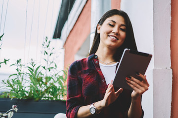 Wall Mural - Cheerful asian hipster girl enjoying leisure outdoors with modern portable pc while receiving positive email from friend, joyful woman watching funny videos on websites connected to 4g internet