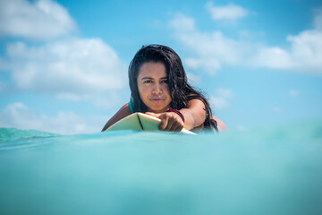 Portrait of surfer girl on white surf board in blue ocean pictured from the water