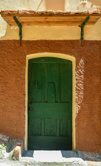 Canvas Print - Close-up of the exterior of an old buidling with a green wooden door on an orange and yellow wall, Italy