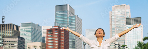 Fotomural Happy asian woman with open arms up to the sky breathing fresh air in city downtown buildings background
