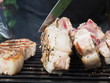 © Владимир Сидоров - a cook in a black apron roasts steaks meat on the bone. grilled pork on the bone. tongs for grilling.