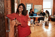 © SuperStock - portrait young ethnic woman standing and leaning on sliding door, coworkers gathered around desk in background