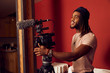 © SuperStock - Portrait of a young ethnic man standing on a film set running motion camera on a tripod with microphone