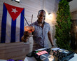 Cuban disc jockey drinking cocktail and playing music on a modern dj turntable mixer equipment.