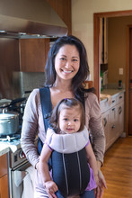 Mother Holding Daughter In Sling In Kitchen