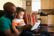 © Tetra Images - Father reading to baby on sofa