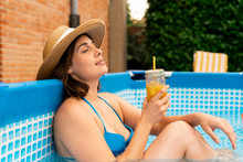 Woman Holding Orange Juice While Relaxing In Inflatable Swimming Pool At Yard