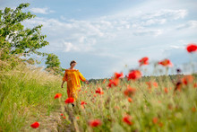 Happy Mature Woman Walking Amidst Poppy Field Against Sky