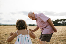 Grandfather Looking At Granddaughter While Standing On Land Against Sky