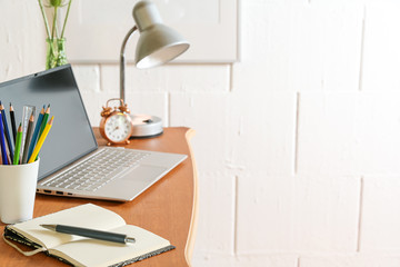 Wall Mural - Wooden desk with laptop, notebook, pencils, lamp and tools against a rough white wall, small home office, copy space, selected focus