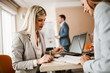© Mediteraneo - Two smiling young businesswomen reading paperwork together while sitting at a boardroom table during an office meeting