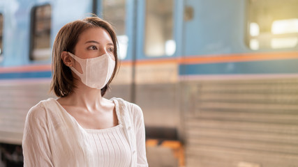 Woman in protective mask wait for the local train on platform at station.