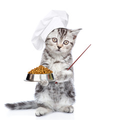 Poster - Kitten wearing chef's hat stands with bowl of dry food and points away on empty space. isolated on white background