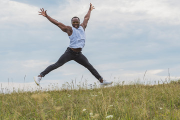 Young and happy man jumping high into the sky on a green meadow