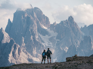 couple of hikers standing and admiring stunning beauty of impressive jagged peaks of cadini di misur