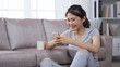 © PRPicturesProduction - asian girl drinking tea and playing games on phone in her leisure time. portrait korean female having fun with mobile games at home. technology and indoor recreation.