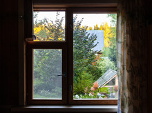 View Of Green Backyard With Well Through Window In Rural House At Summer Sunset