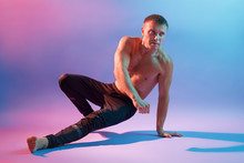Gymnast Training To Keep His Body Balance While Being Photographed Against Neon Background, Dresses Black Pants, Looking Aside, Demonstrates His Perfect Shapes.