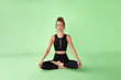 © RedUmbrella&Donkey - Yoga as a way to healthy and balanced life. Brown-haired lady in black gym outfit is sitting in half lotus pose with closed eyes. Indoor photo on the green backdrop.