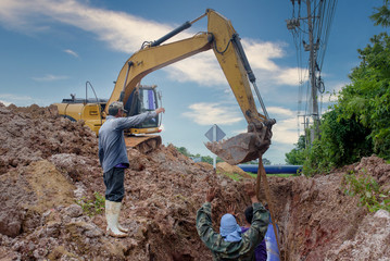 Asian workers inspect a massive sewer buried underground at a construction site. The excavator is empty the water pipe.