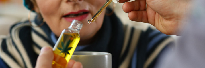 Wall Mural - Close-up of elderly woman receives sedative drops from doctor. Glass bottle with leaf sign. Prescription herbal meds. Traditional medicine cannabinoid oil and healthcare concept